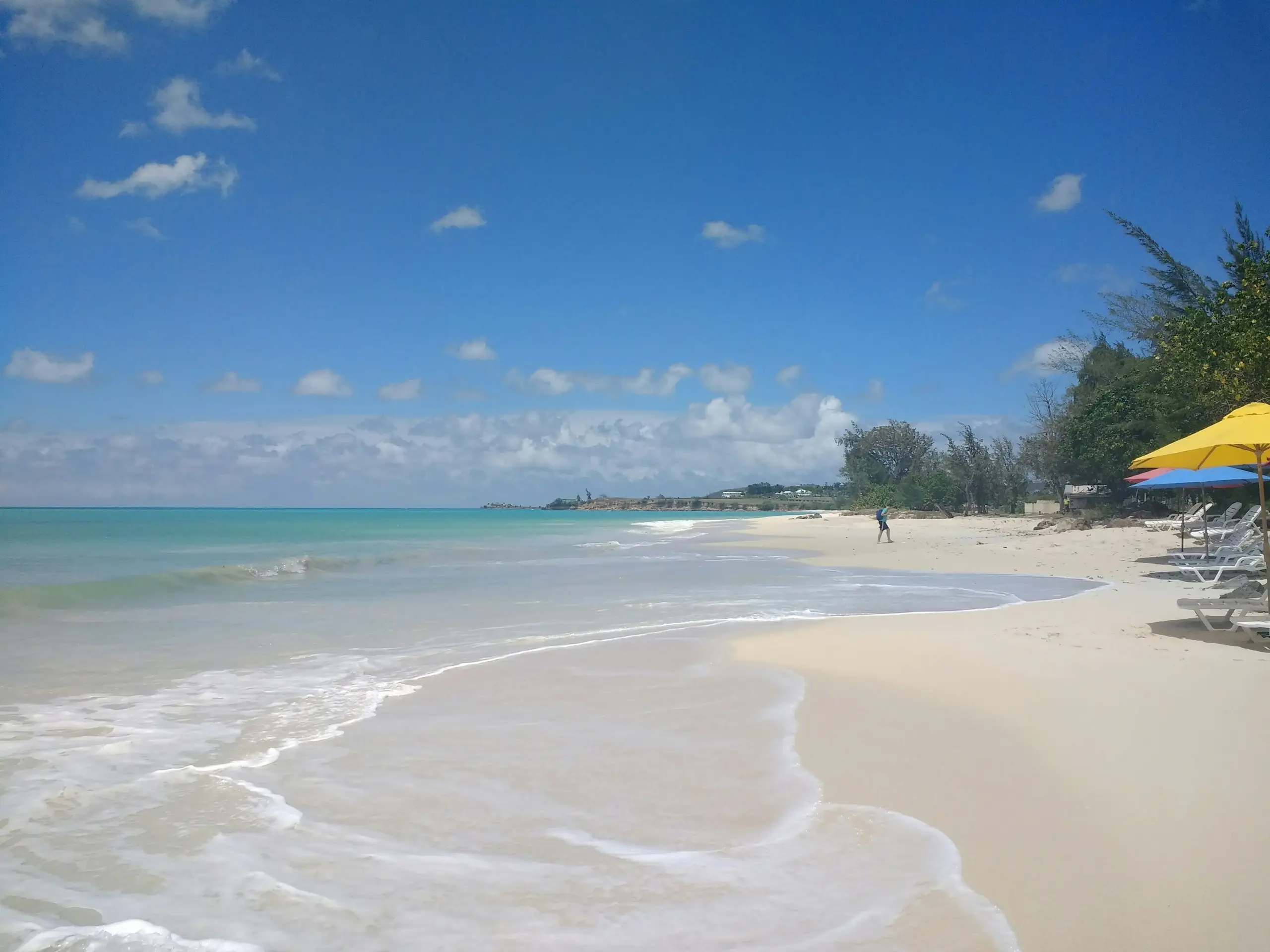A quiet white-sand beach with turquoise water and bright parasols, Antigua