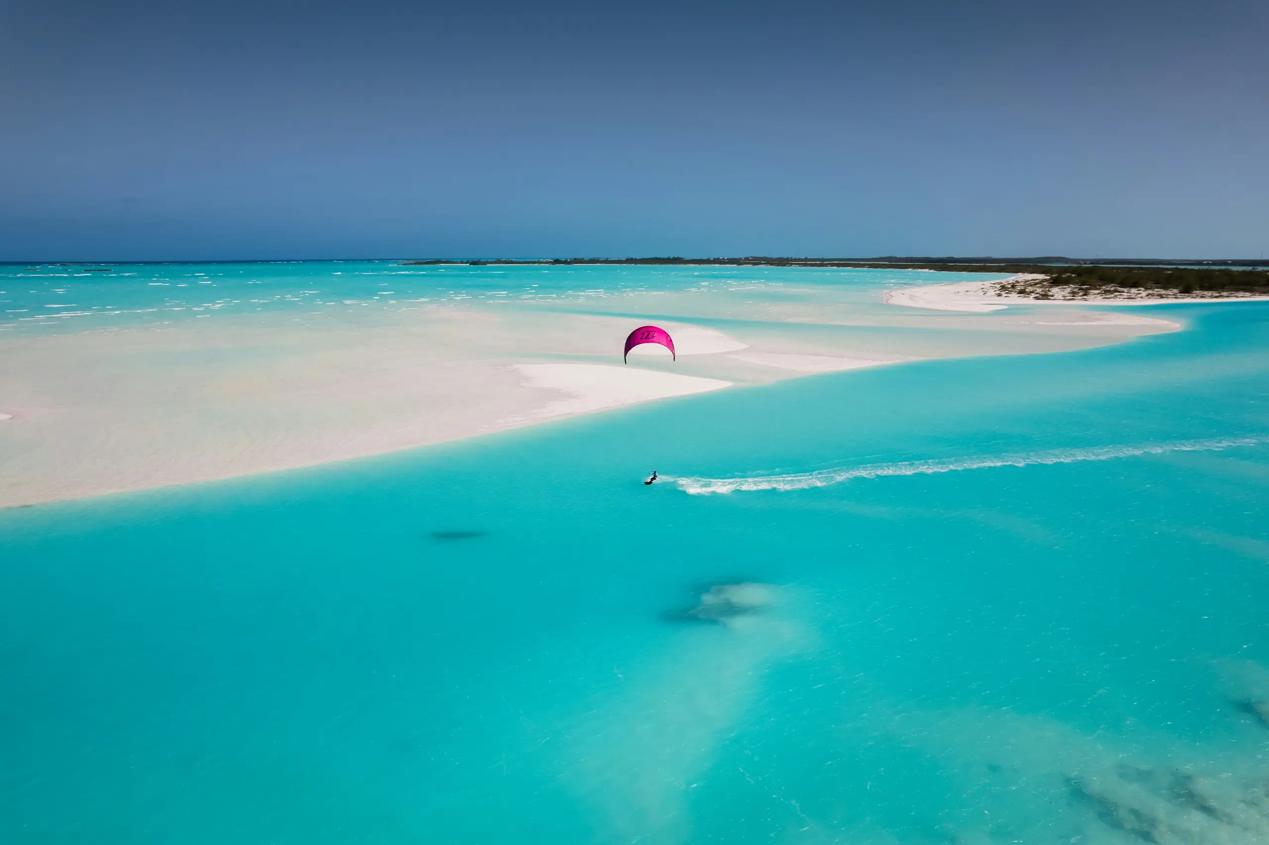 A kitesurfer skimming a turquoise lagoon beside a white sandbar, Freeport, Bahamas