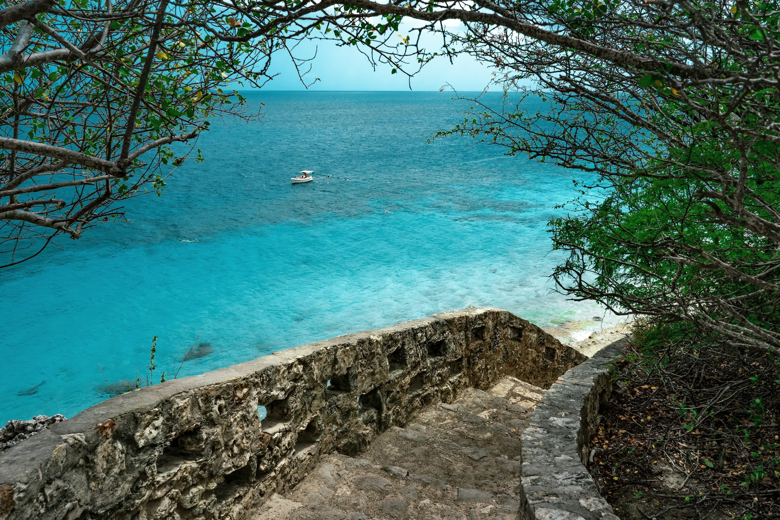 A coral-stone stairway framed by trees above a small boat on Bonaire's turquoise water