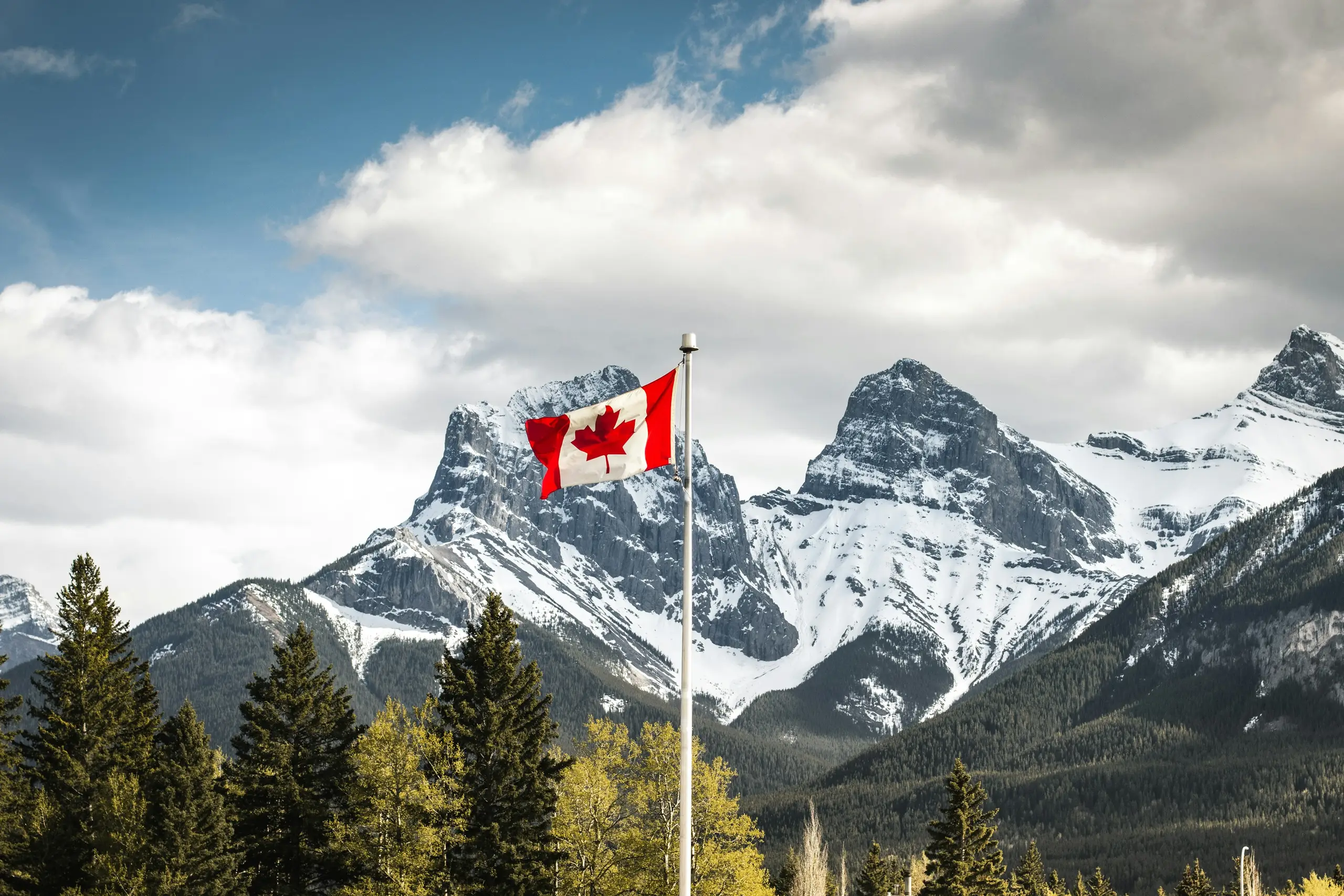 A Canadian flag flying before the snow-capped Three Sisters peaks at Canmore, Alberta