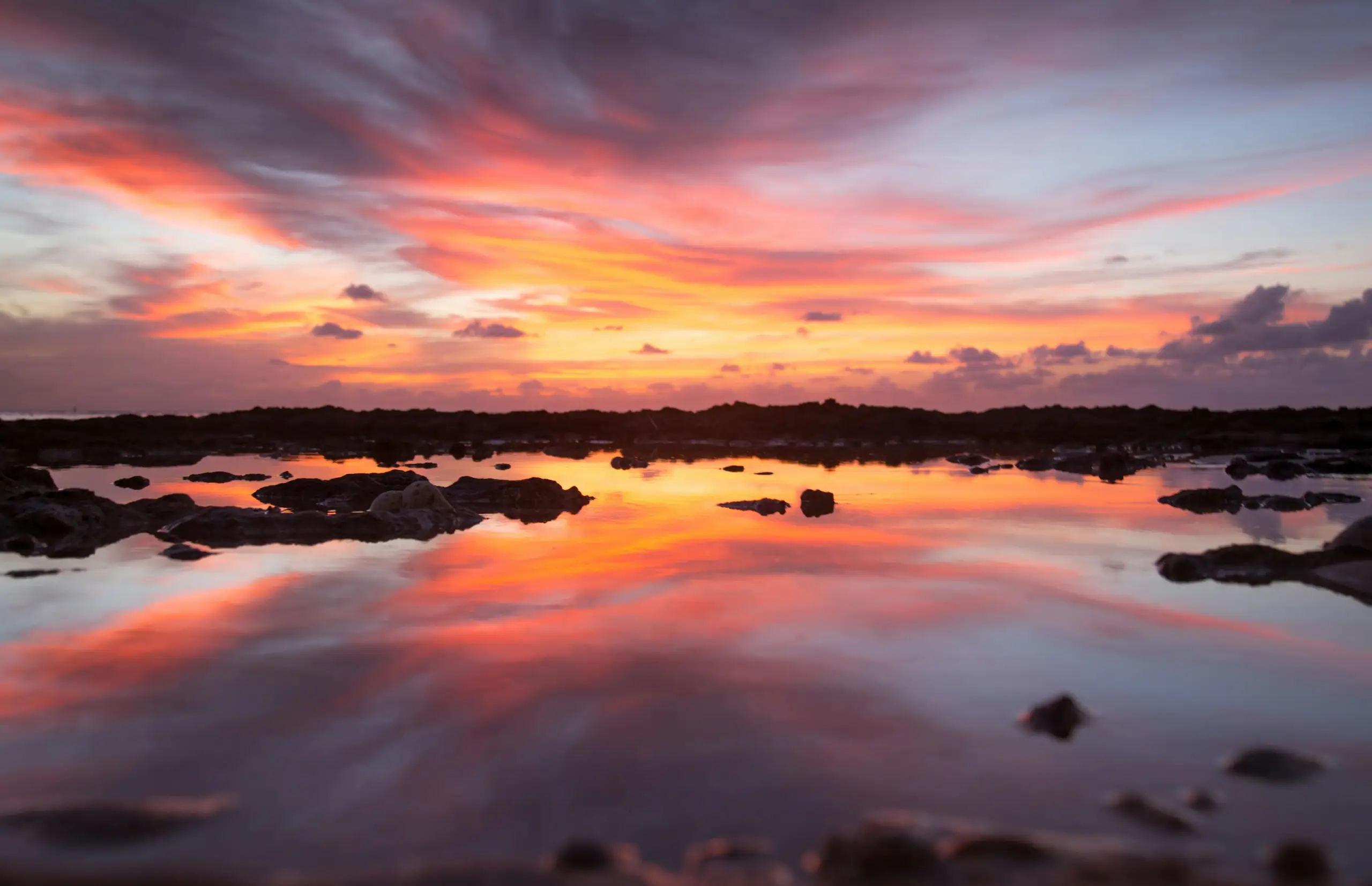 A vivid pink and orange sunset reflected in rocky coastal tide pools, Grand Cayman