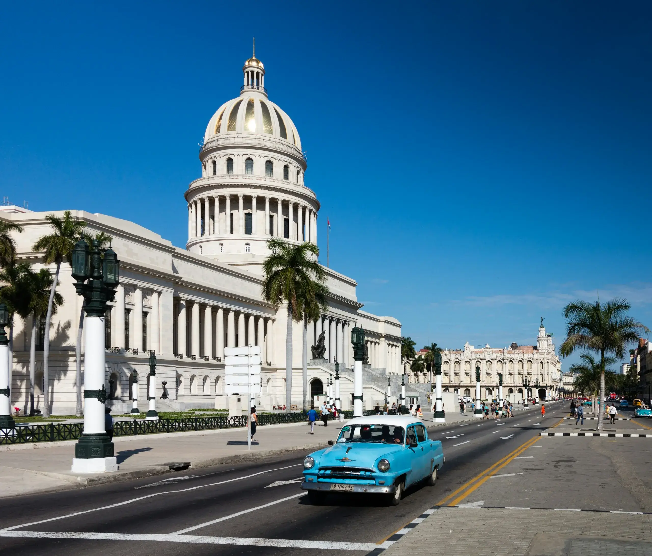 A turquoise classic car passing El Capitolio in Havana