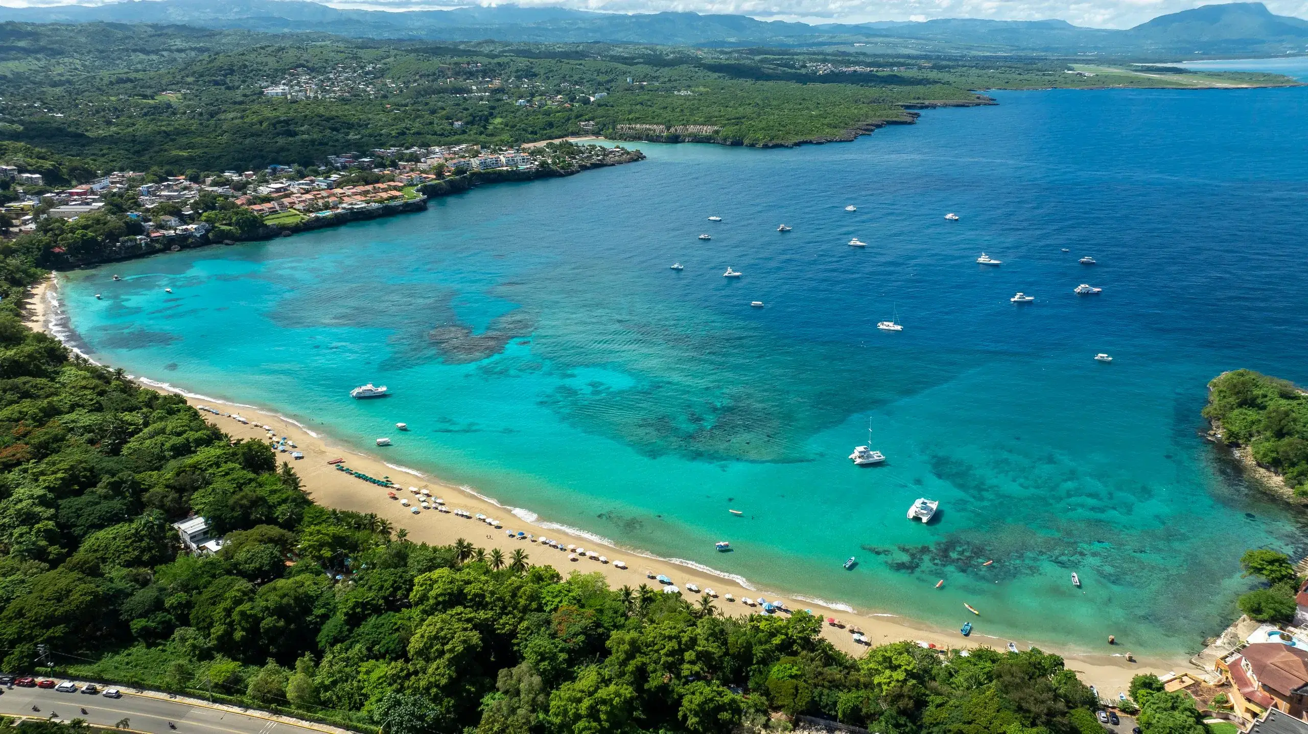 Aerial view of a turquoise bay and curved beach with boats near Sosúa