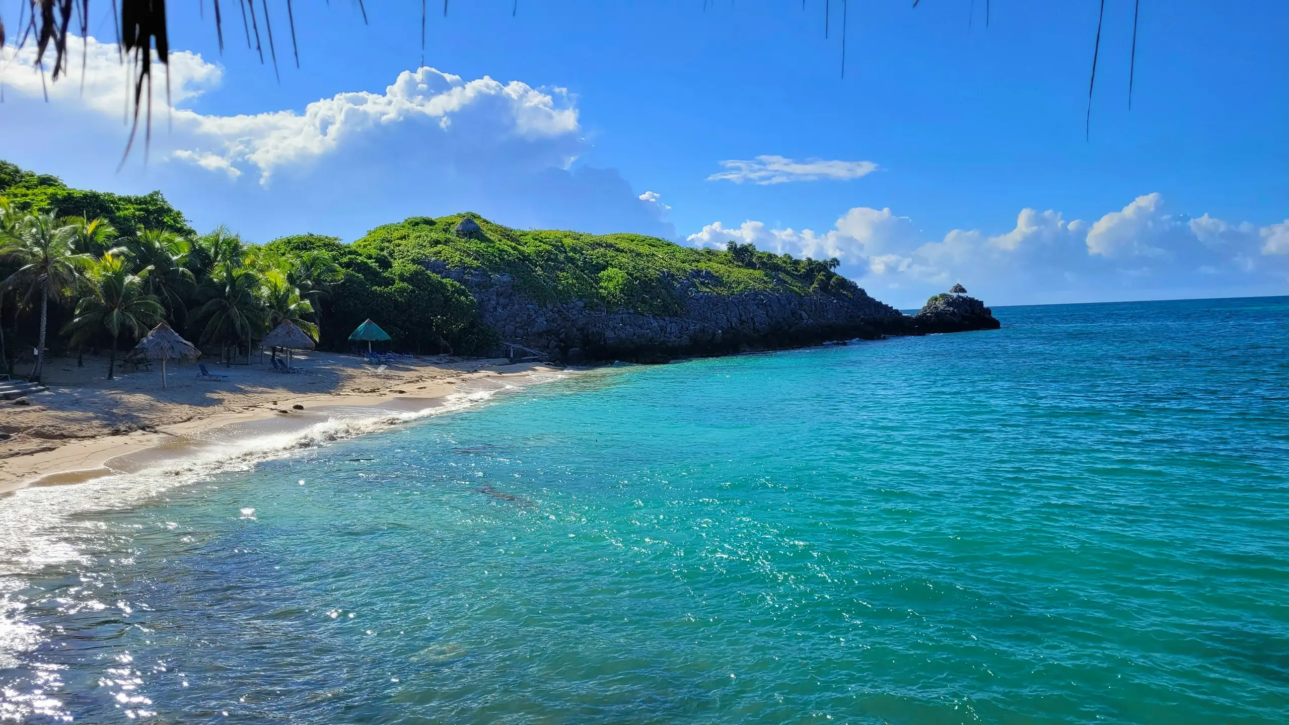 A quiet cove with thatched parasols, palms and clear turquoise water, Roatan, Honduras