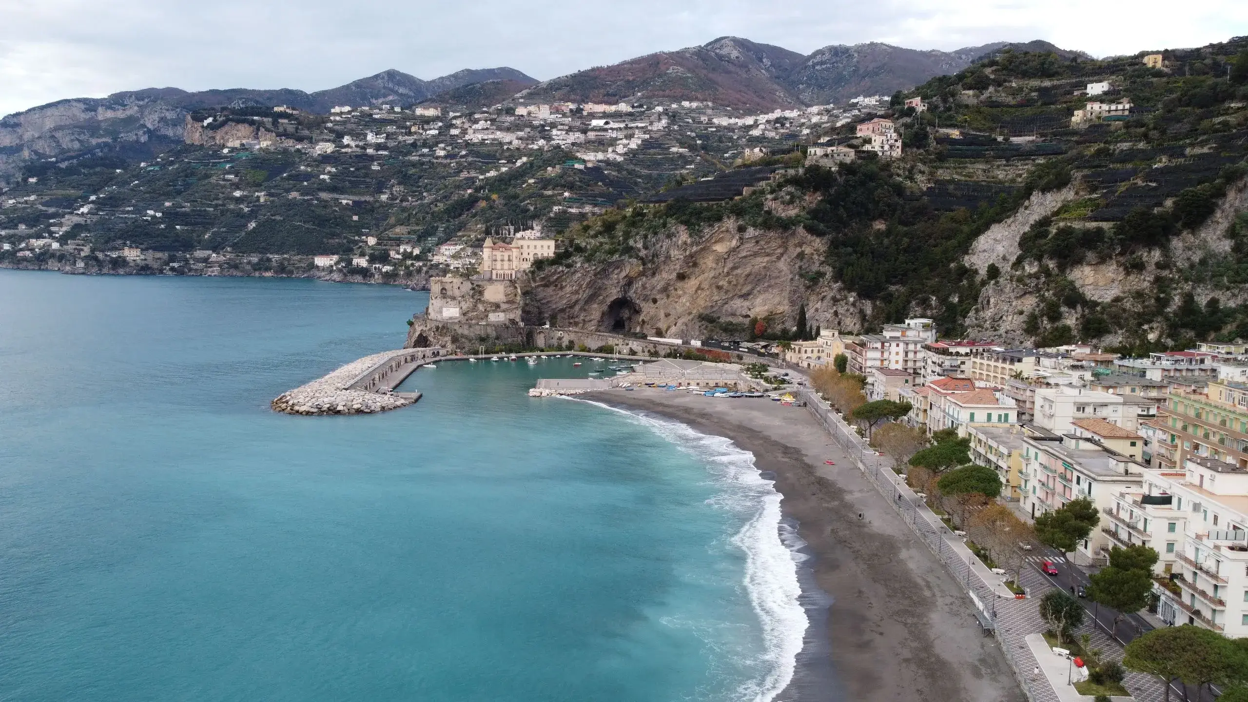 Maiori's dark-sand beach curving to the harbour and Torre Normanna, with terraced Amalfi Coast hills behind