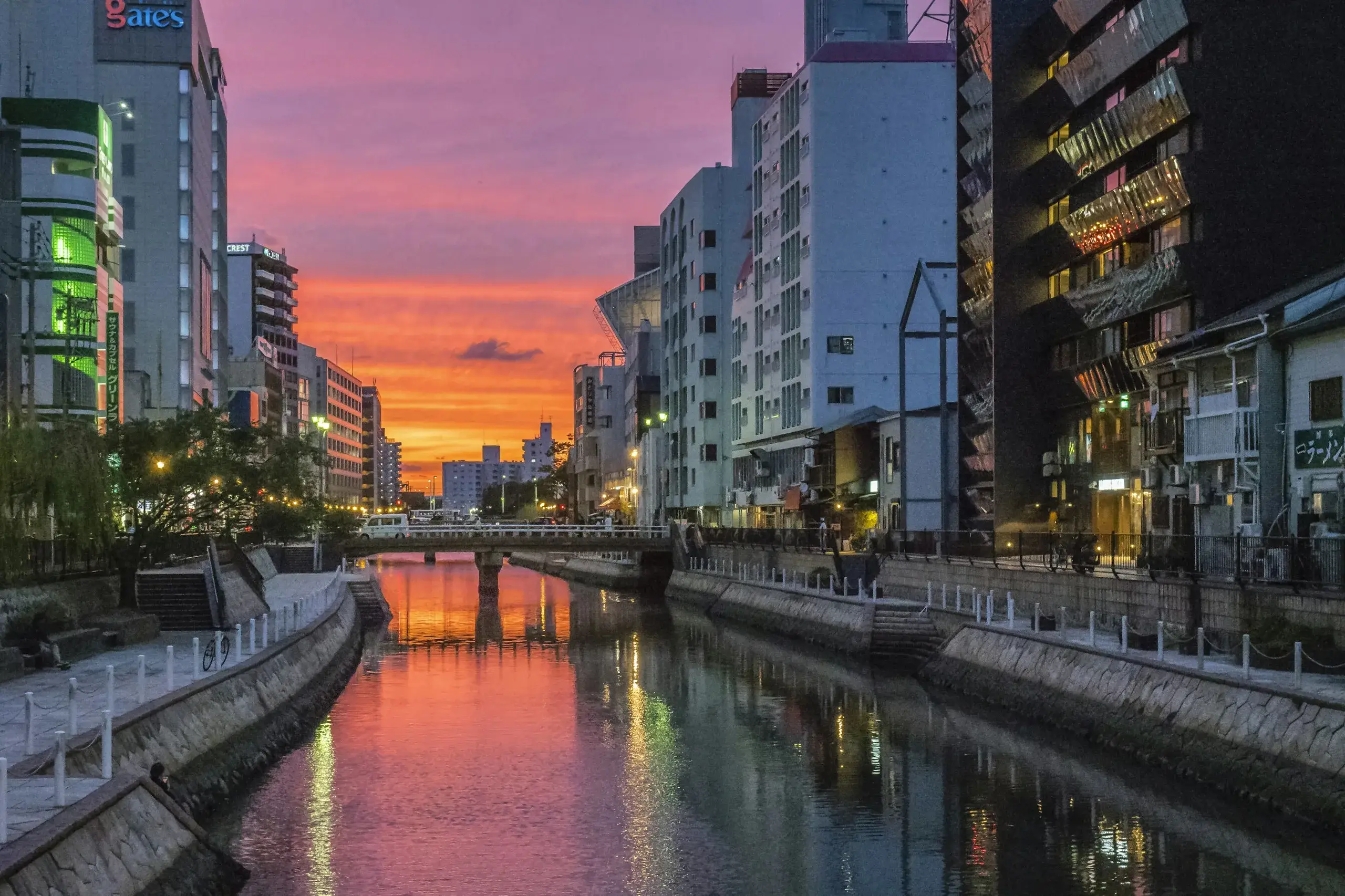 The Naka River at sunset in Nakasu, Fukuoka, lined with city buildings and a low footbridge