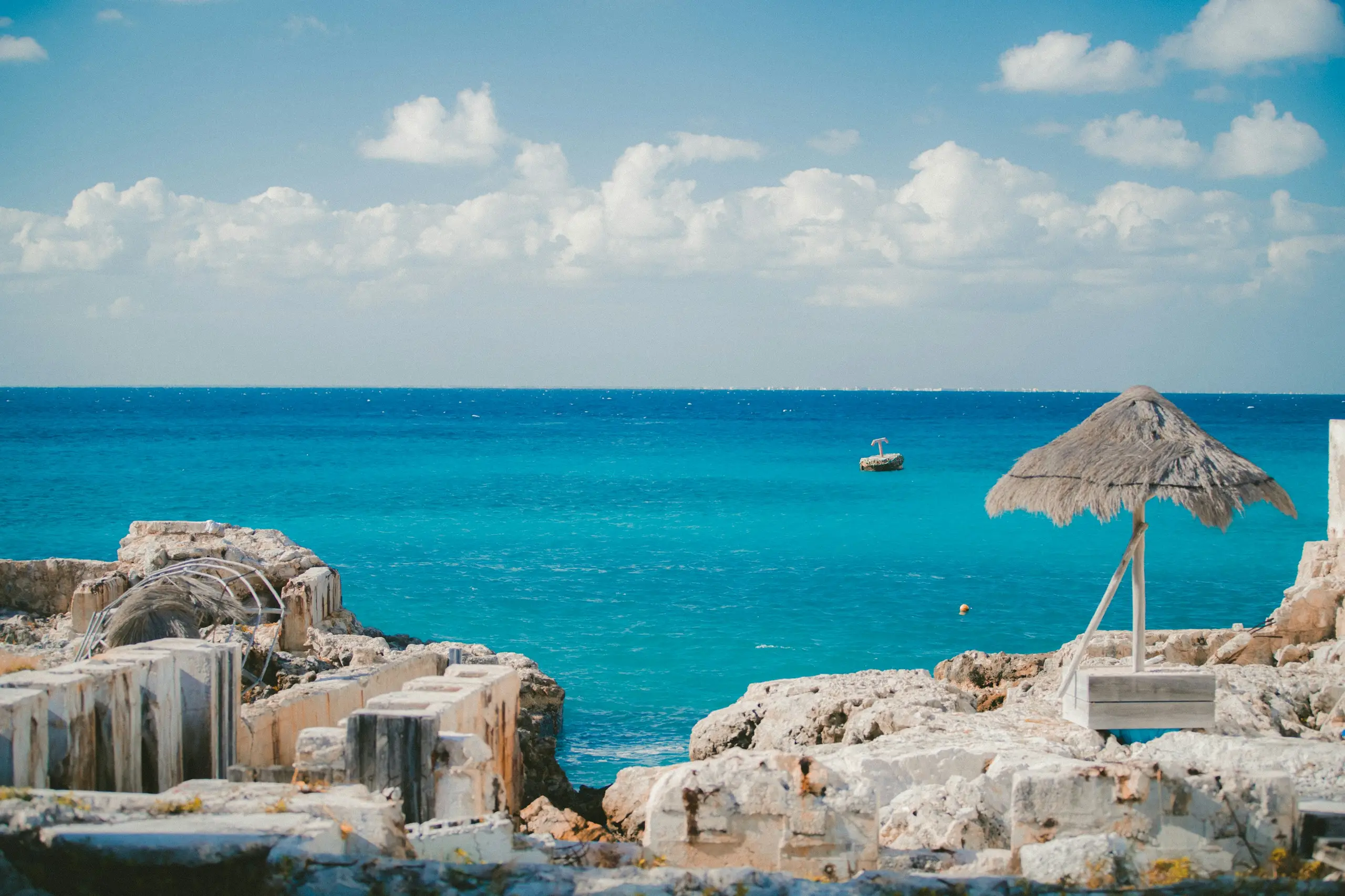 Turquoise Caribbean water beside weathered limestone rocks with a thatched palapa, Cozumel, Mexico