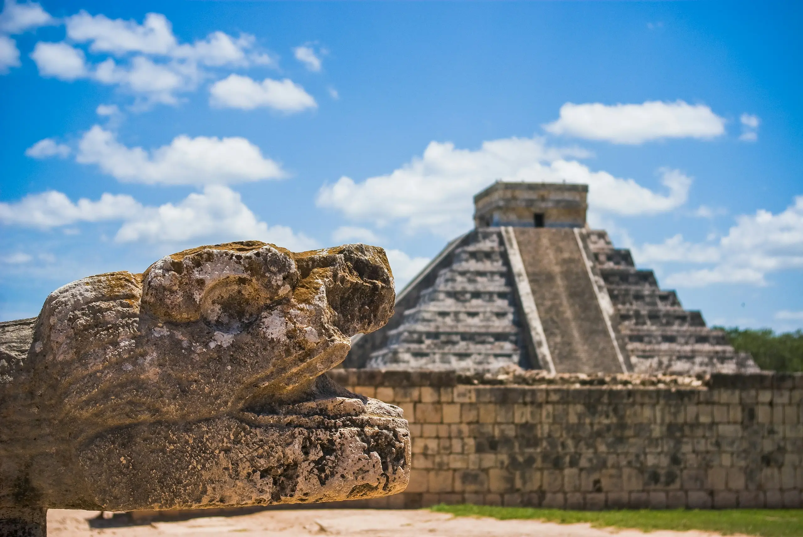 A Maya pyramid rising above stone ruins under a blue sky