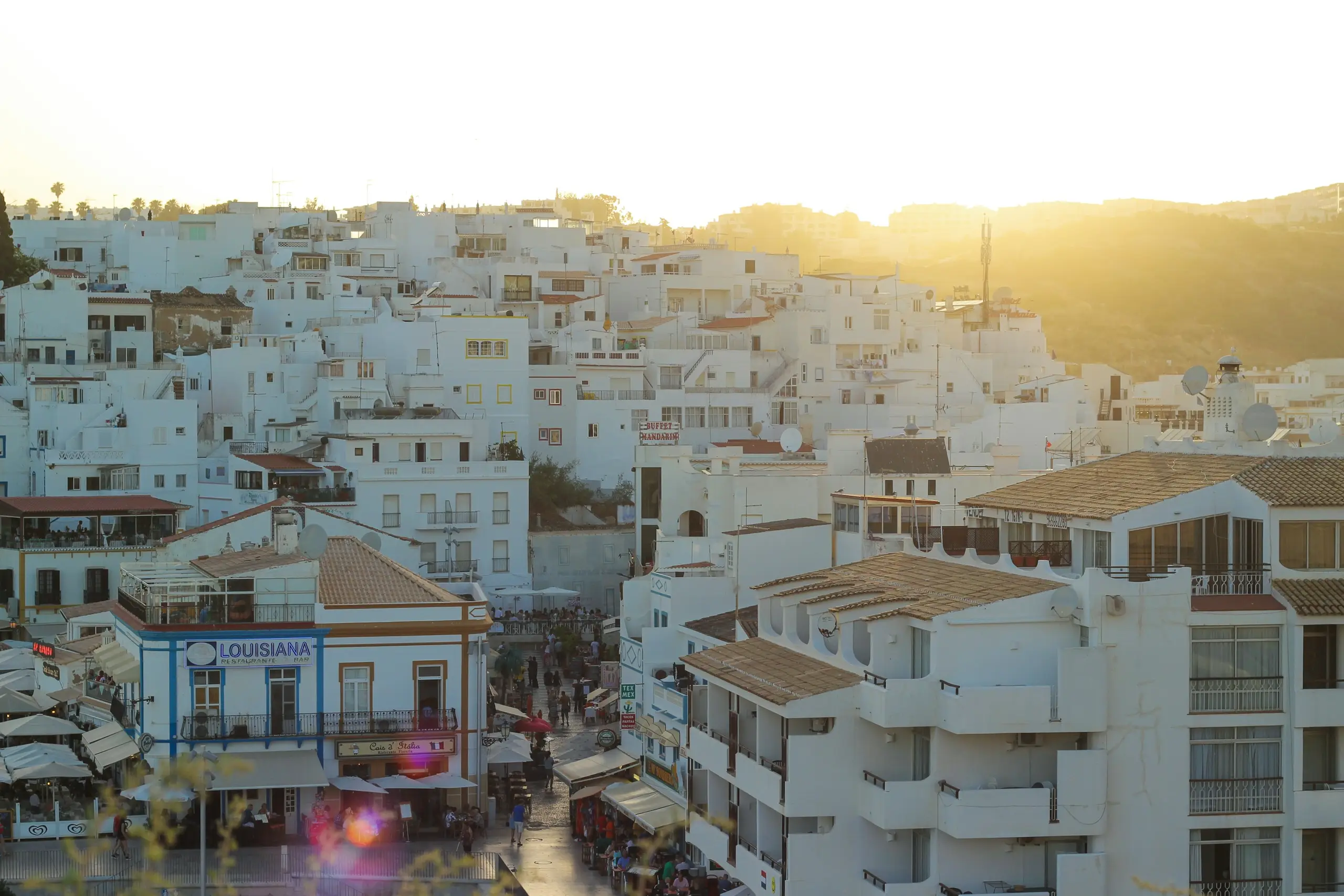 Whitewashed old-town houses stacked on the hillside above the restaurants at golden hour, Albufeira, Portugal