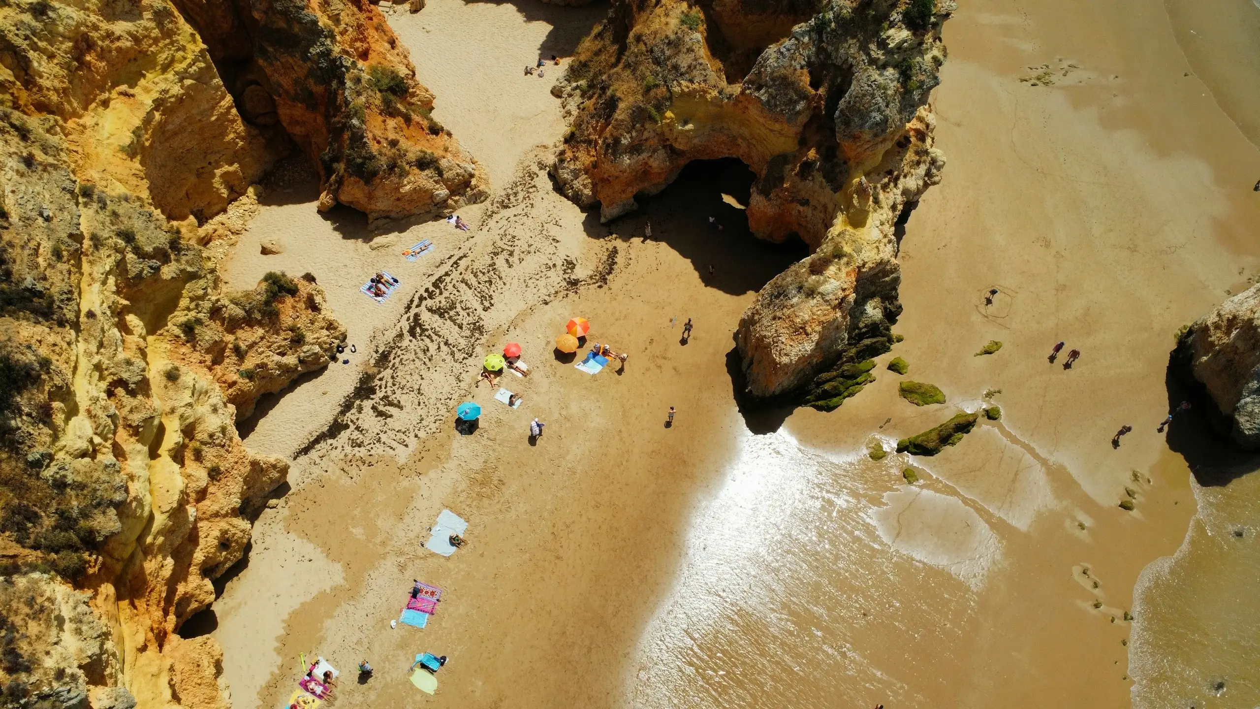 An aerial view of golden Algarve cliffs and sandy coves dotted with parasols, Alvor, Portugal