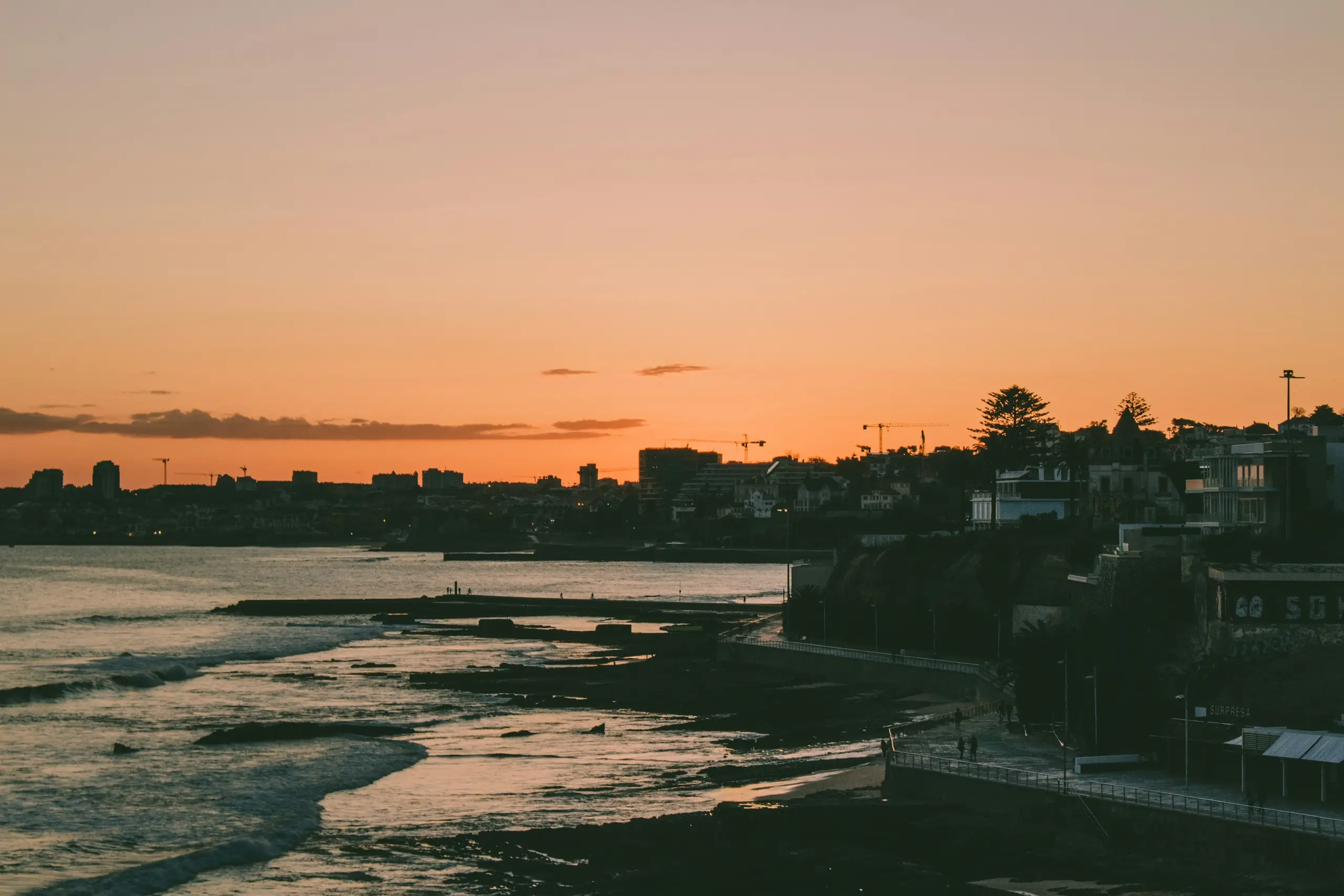 The Estoril coastline and seafront promenade under a warm orange sunset, Portugal