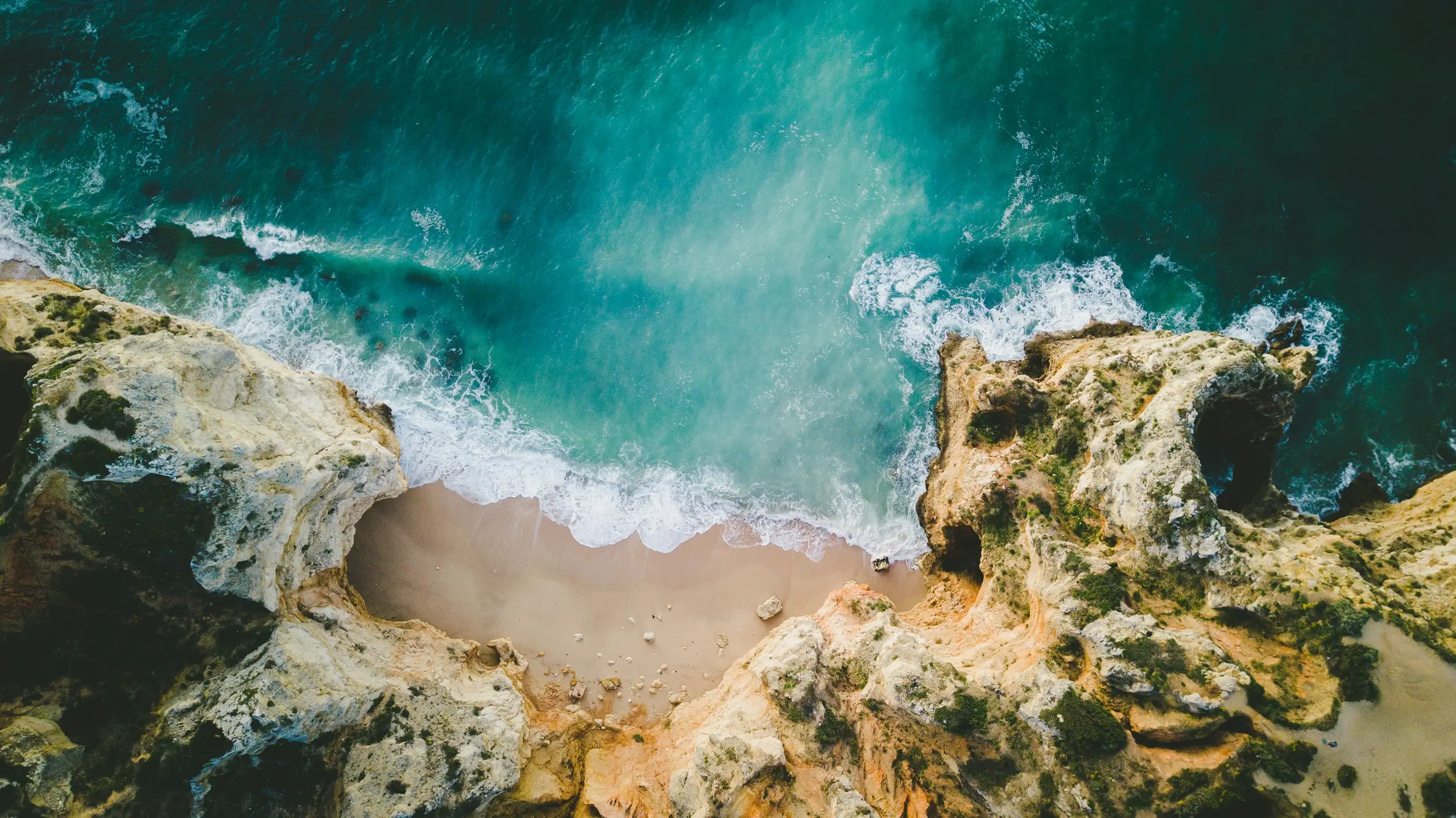 An aerial view of golden cliffs enclosing a sandy cove and turquoise surf, Lagos, Portugal