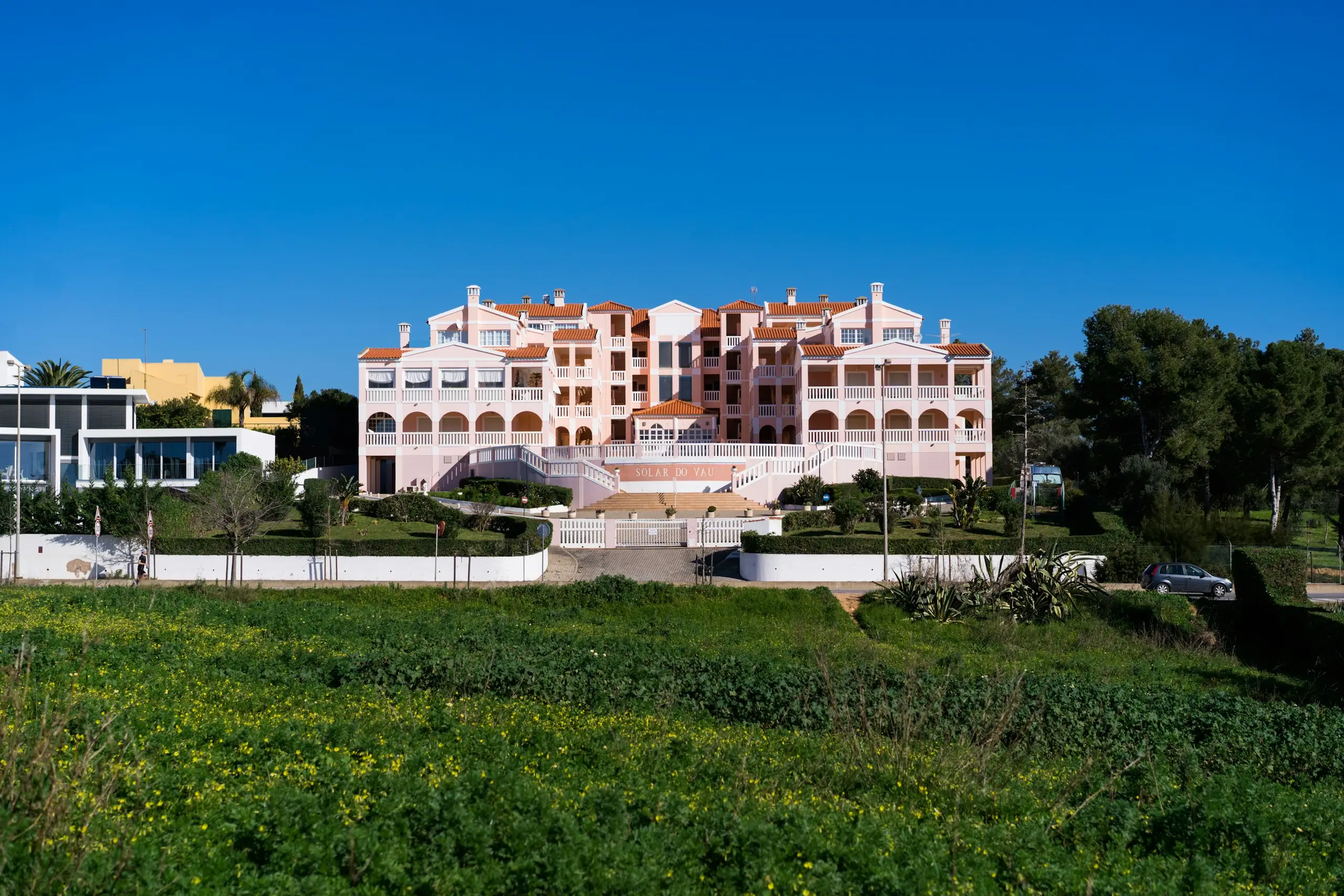 A pink low-rise building beyond a green field under a clear blue sky, Portimao, Portugal