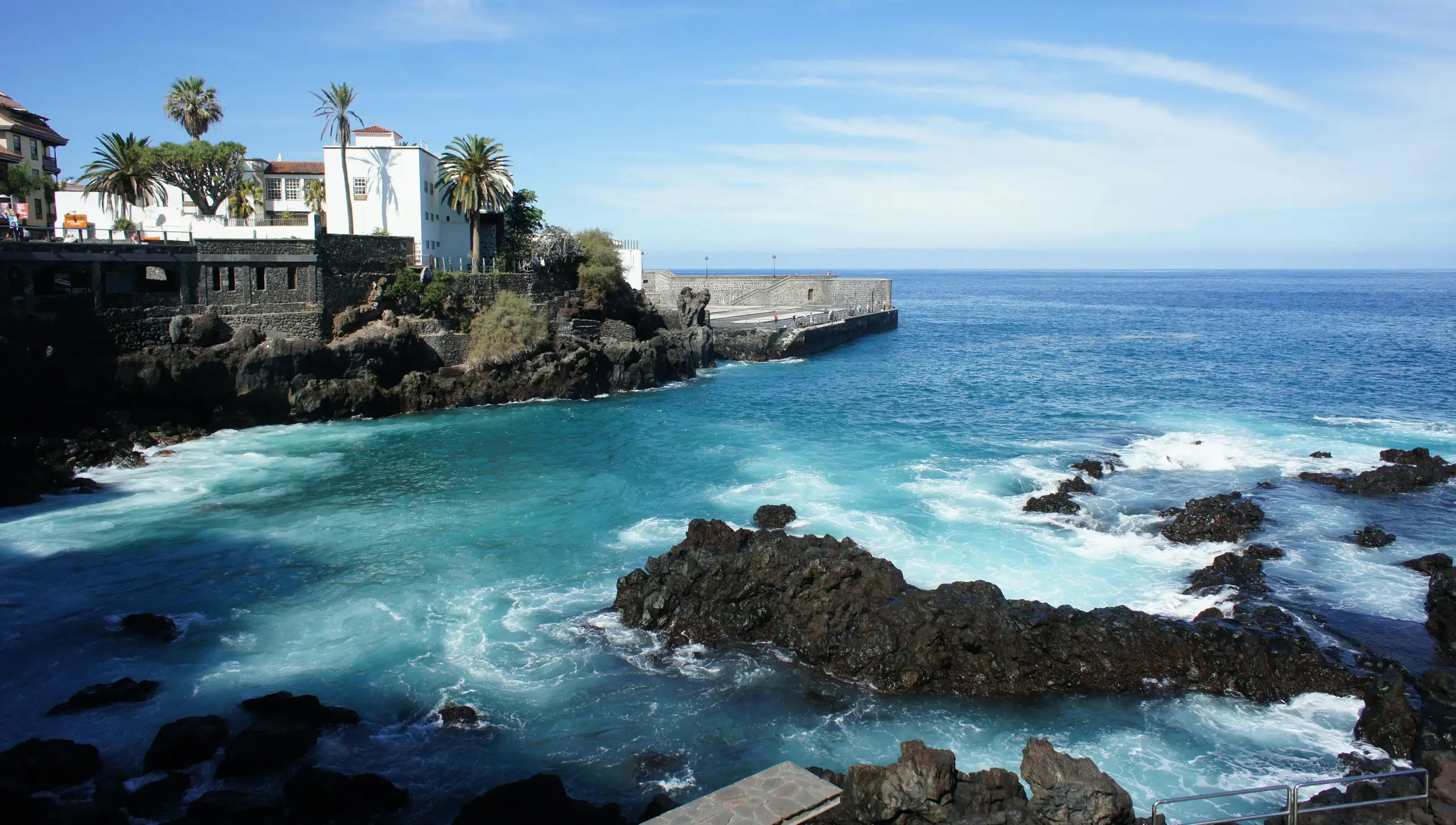 Turquoise surf breaking over black volcanic rocks below the whitewashed town, Puerto de la Cruz, Tenerife