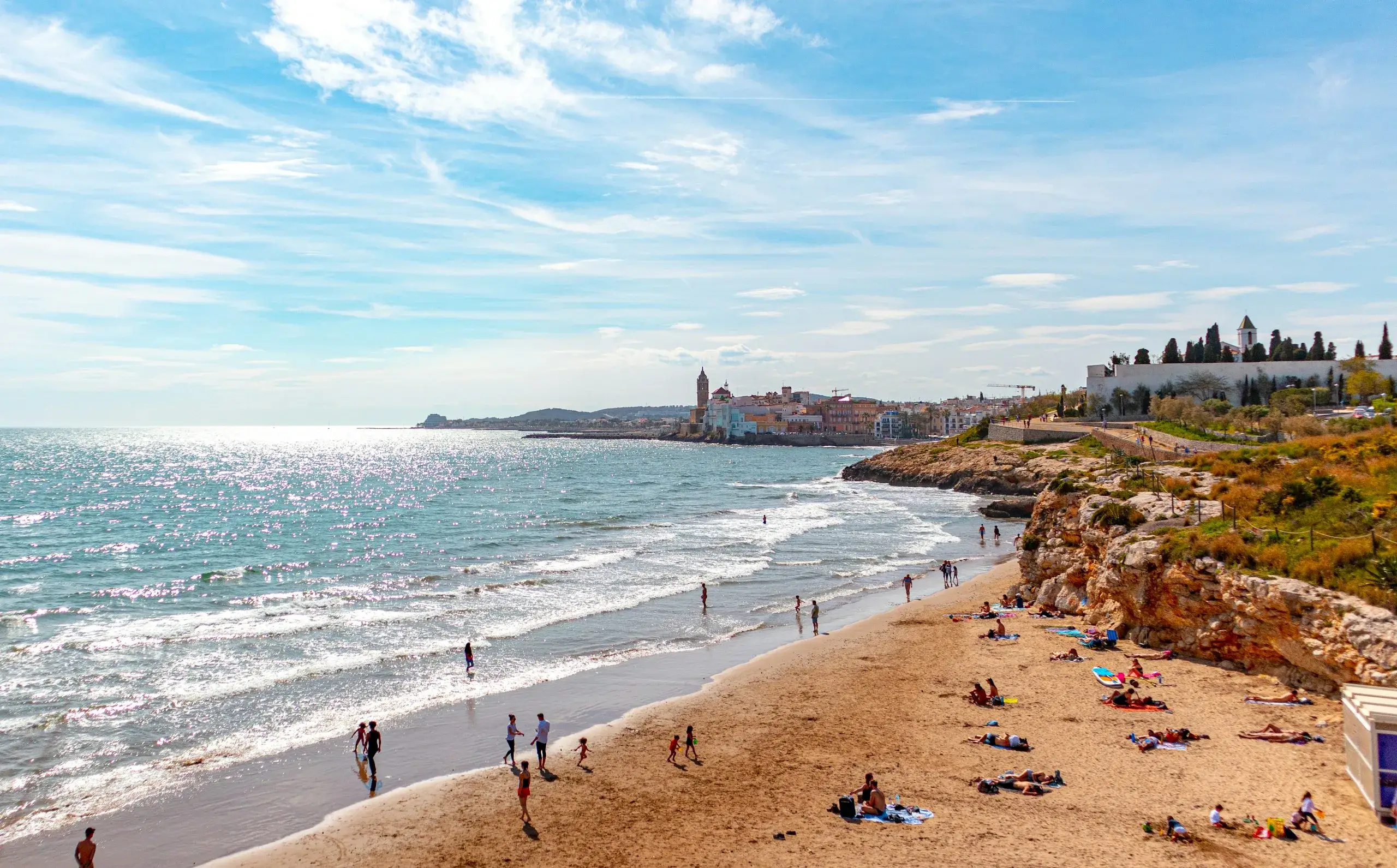 Waves rolling onto a sunny beach with Sitges old town in the distance