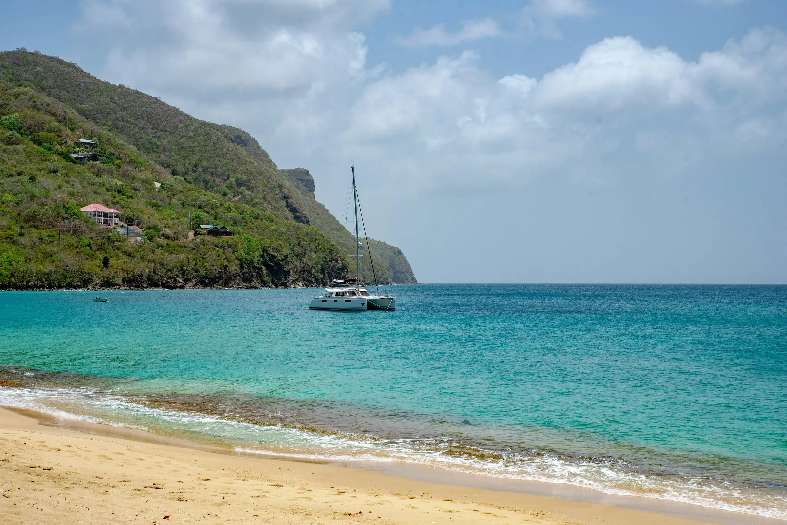 A catamaran anchored in a turquoise bay below green headlands, Bequia, St Vincent and the Grenadines