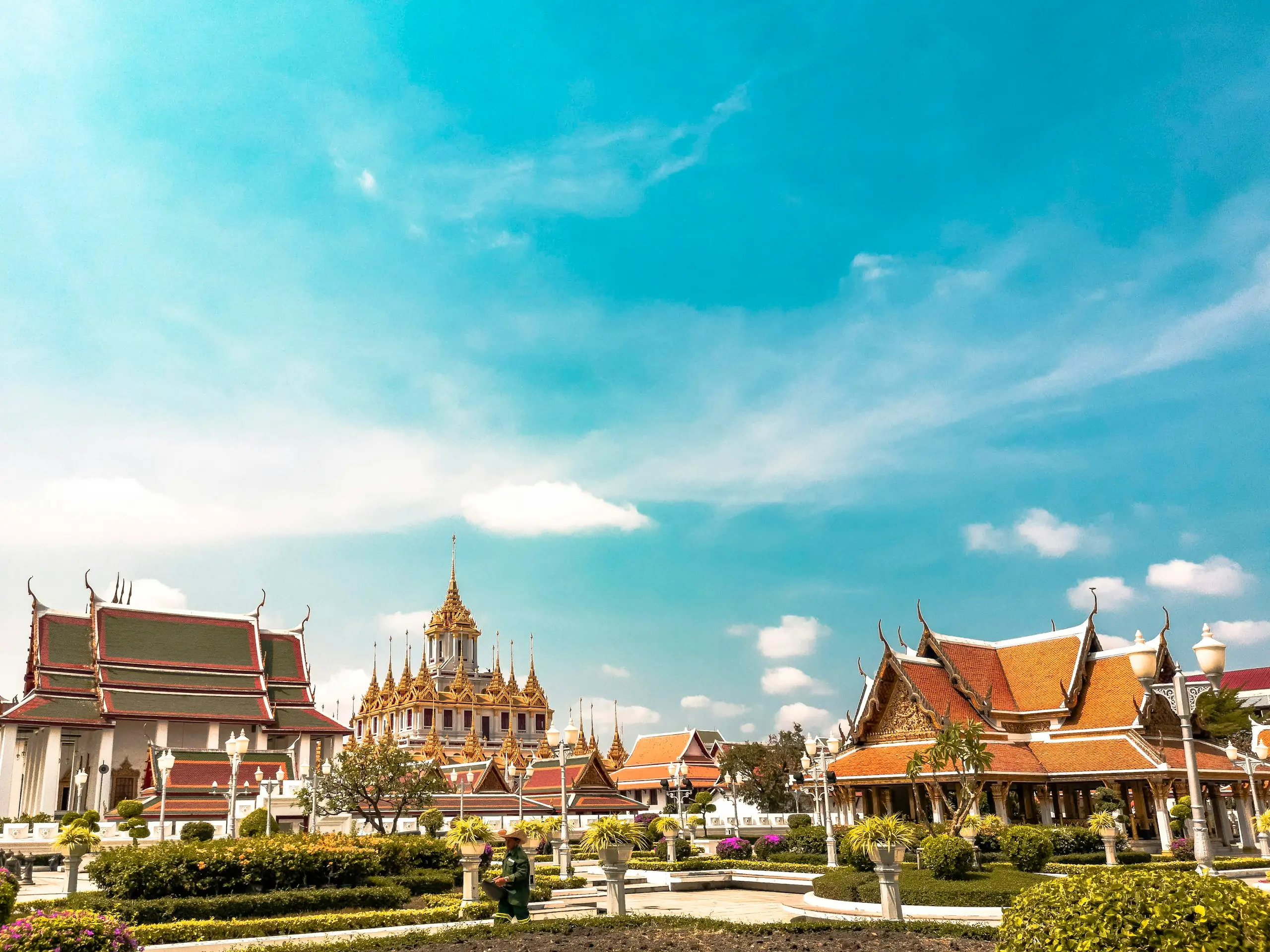 Golden temple spires and gardens under a bright sky, Bangkok