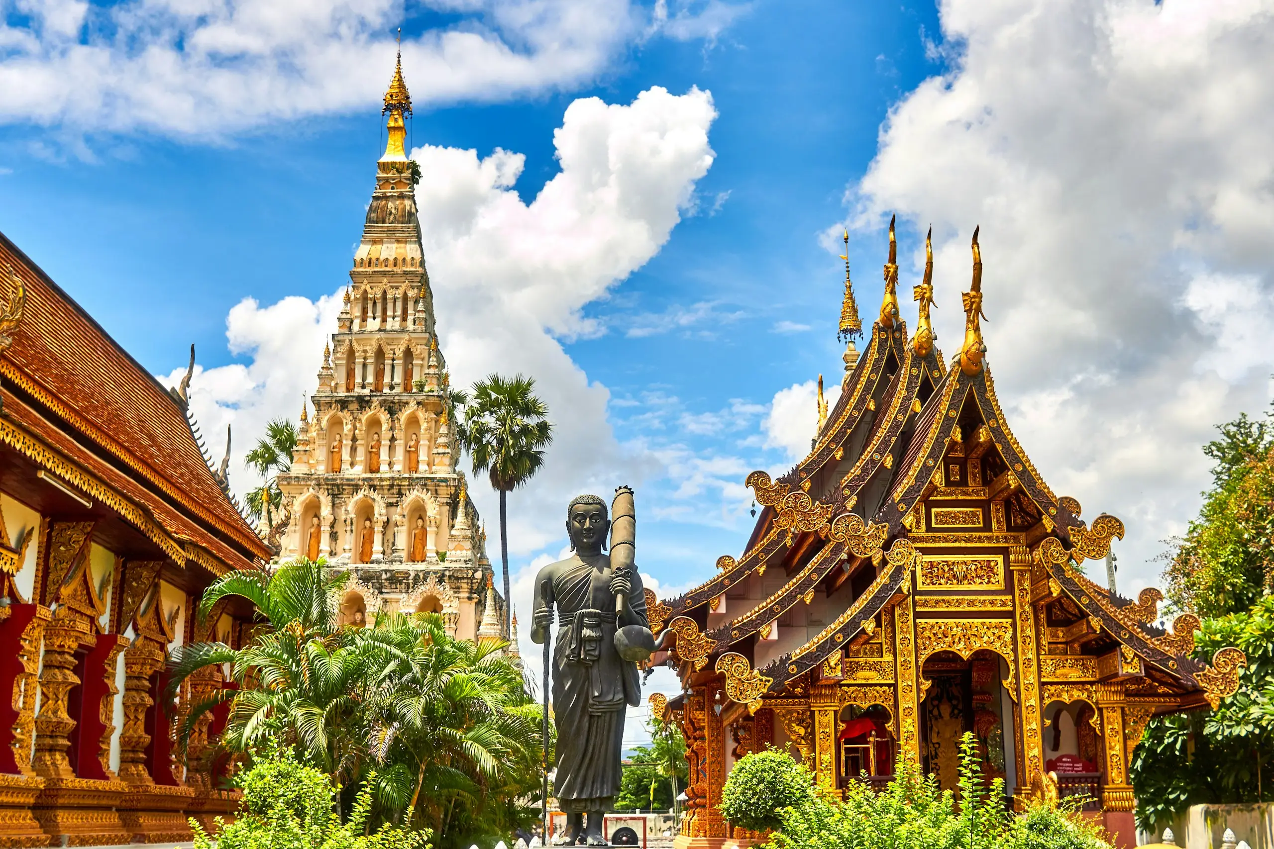 Ornate golden Thai temple roofs and a spire under a blue sky