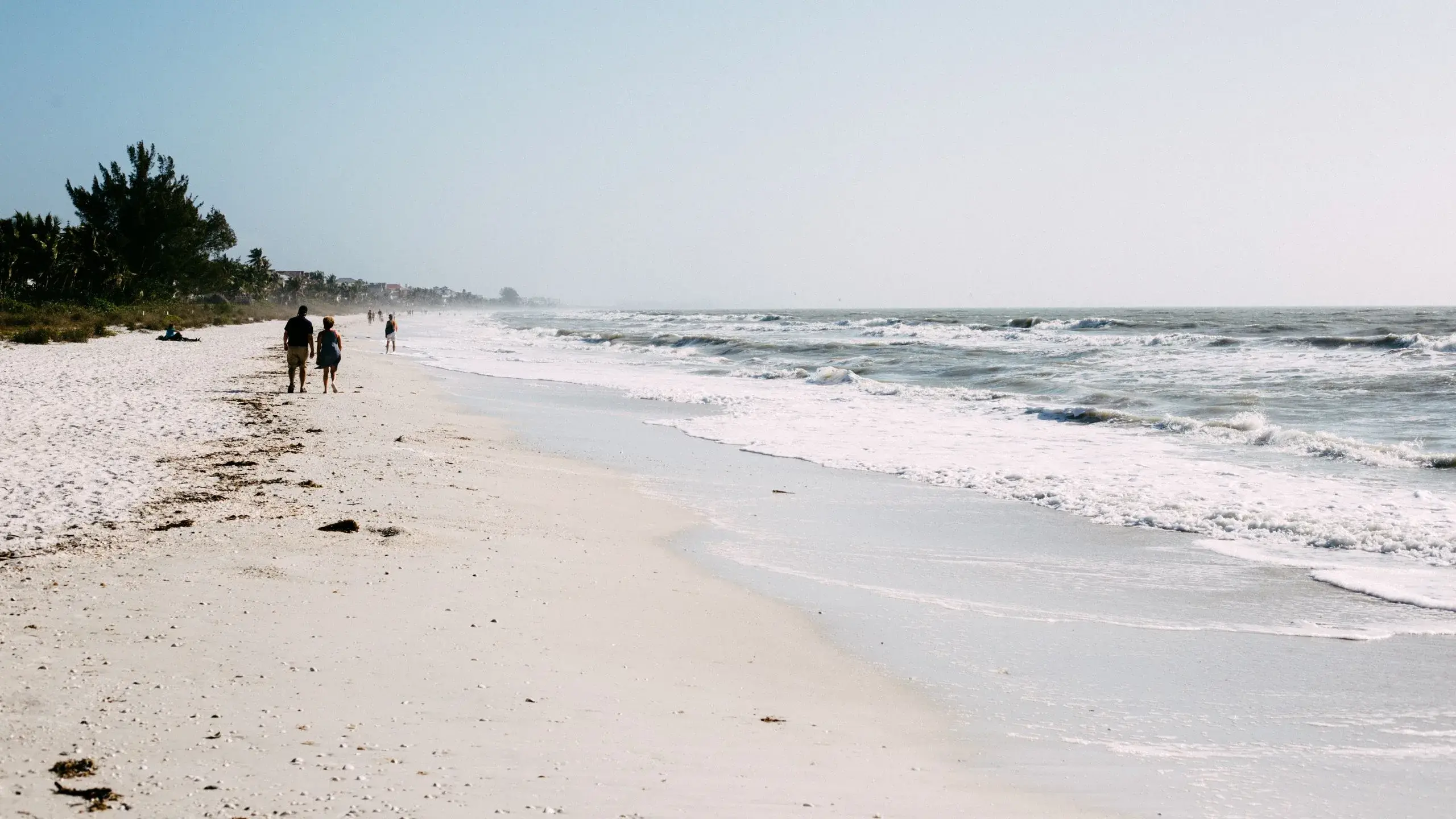 People strolling along a wide white-sand beach as waves roll in on the Gulf coast