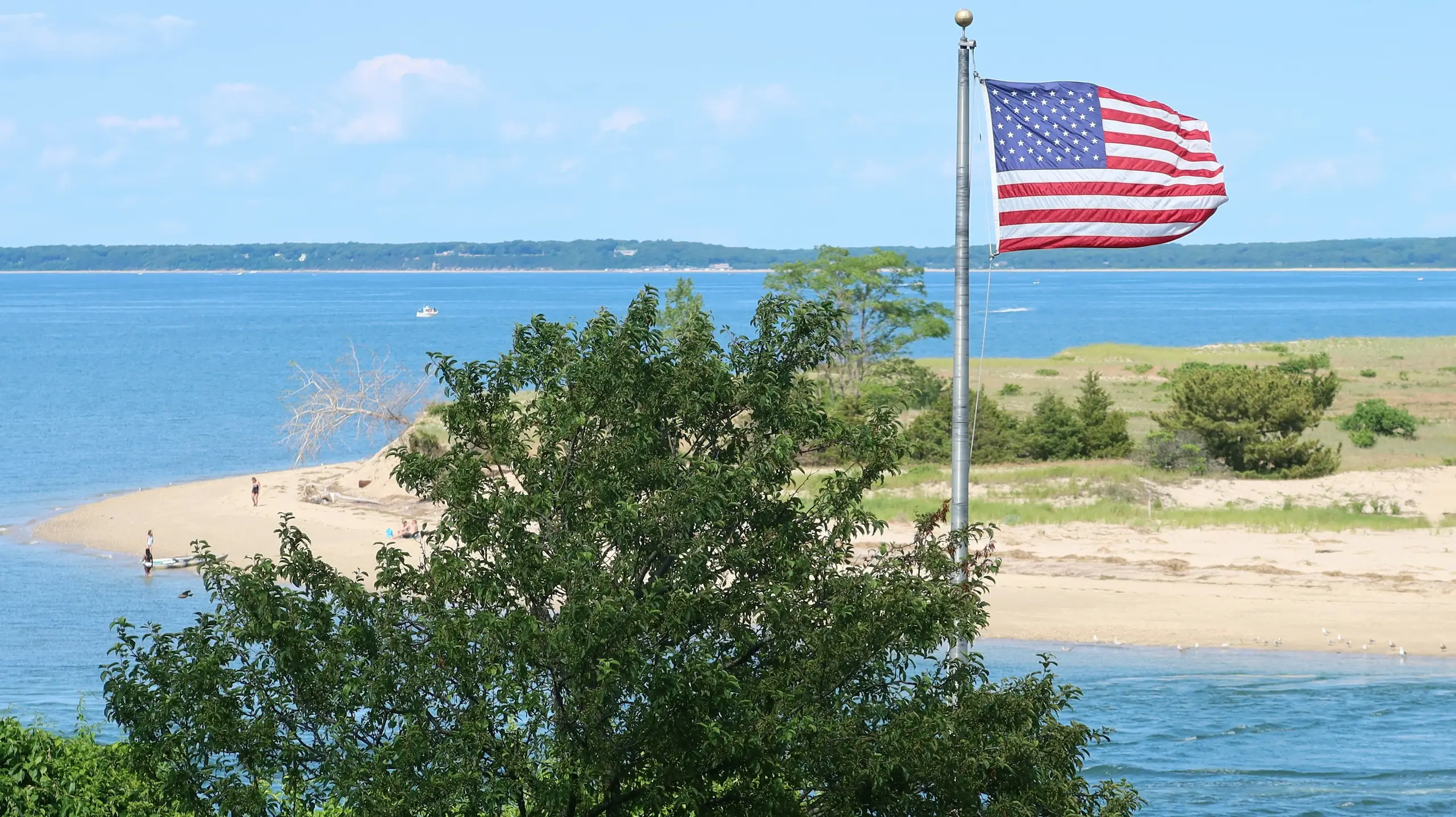 A US flag flying above a sandy spit and calm blue bay, Cape Coral, Florida