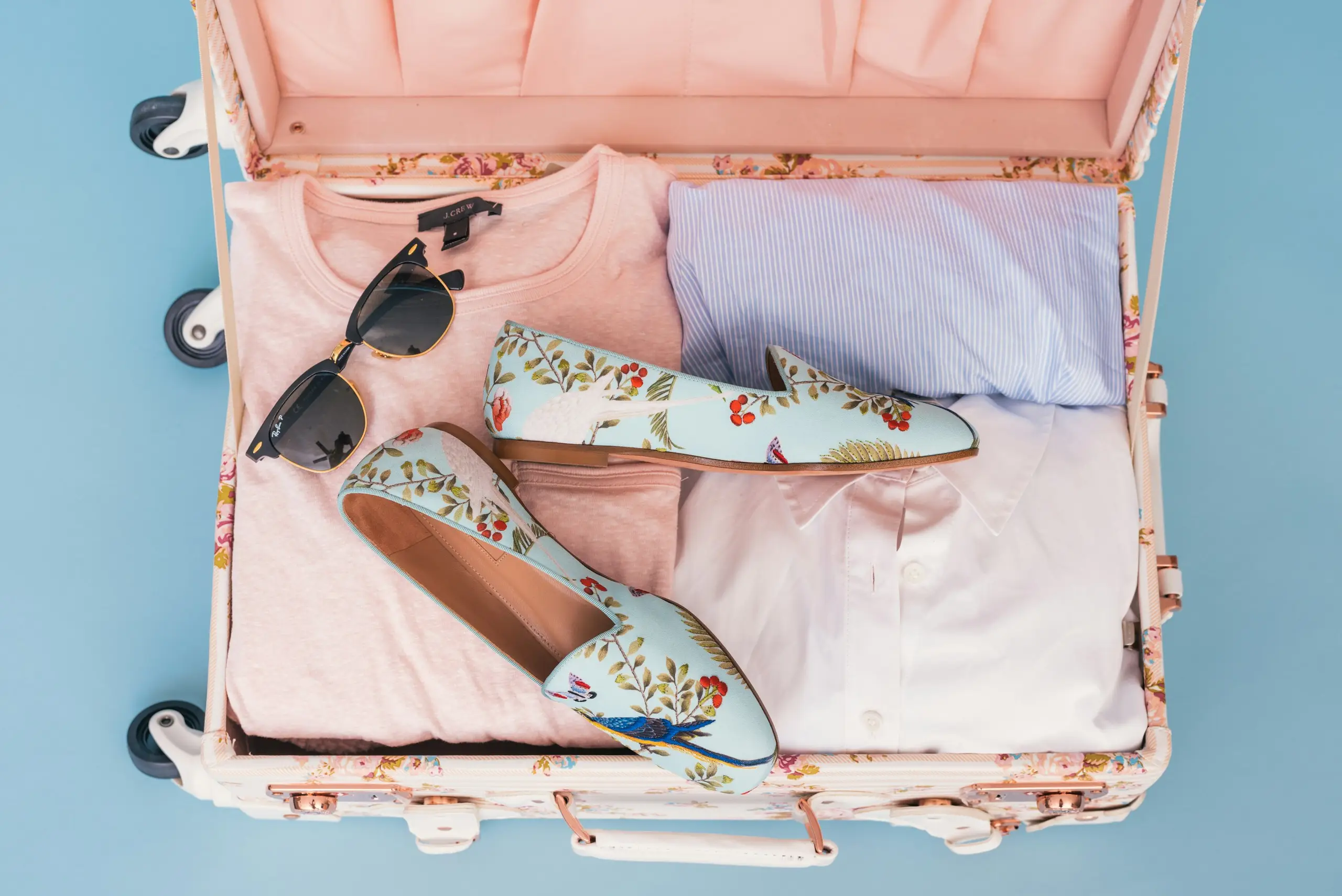 Overhead view of an open suitcase packed with clothes, sunglasses and shoes