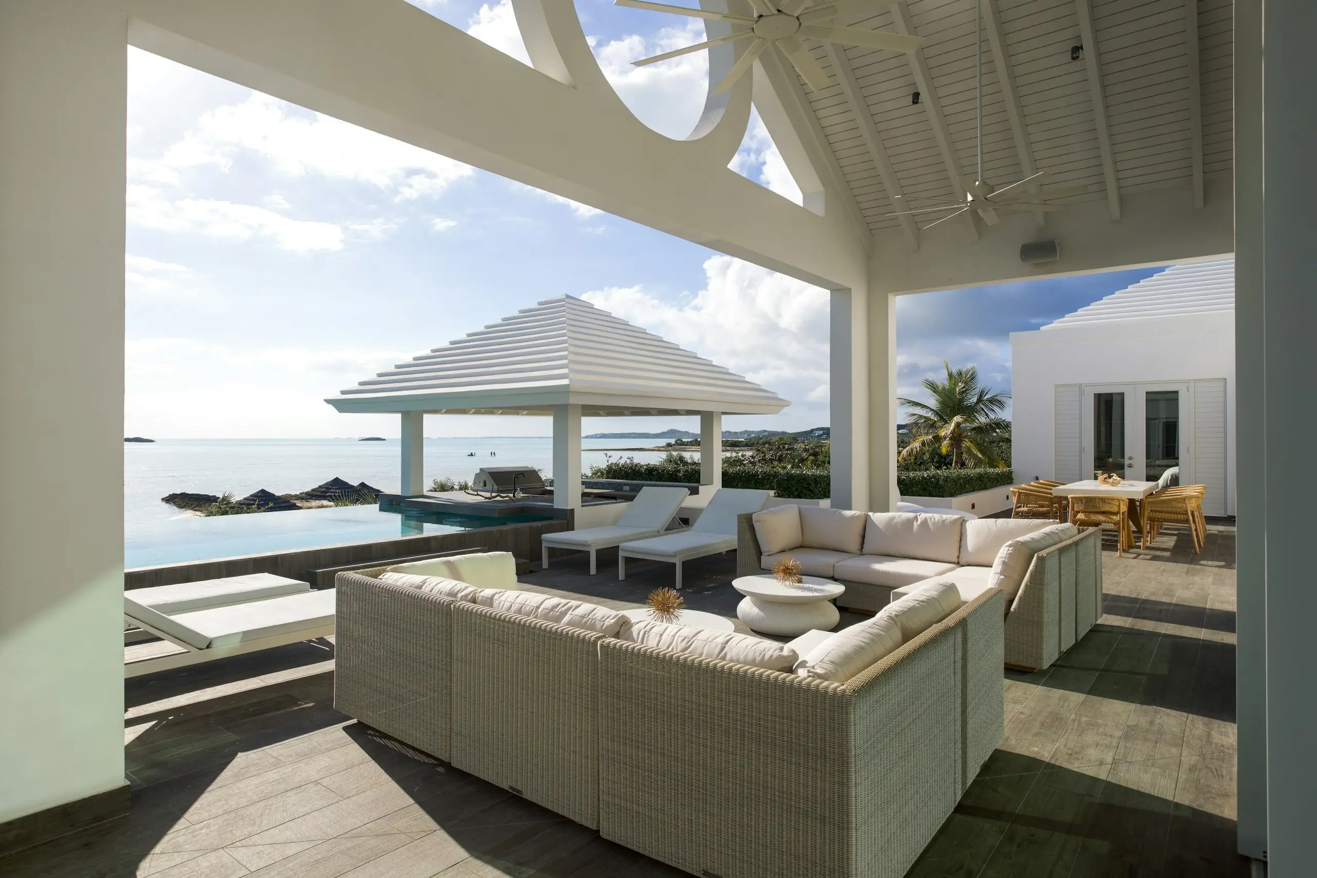 A covered villa terrace with white sofas overlooking an infinity pool and the turquoise ocean
